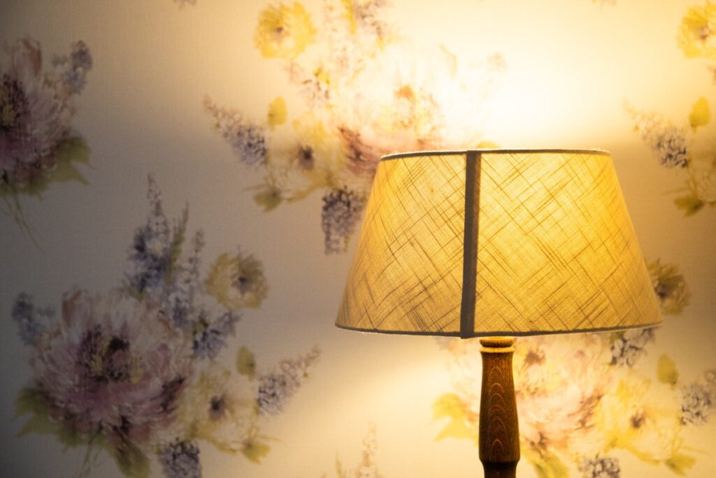Un abat-jour avec une lampe allumée et du papier peint floral
