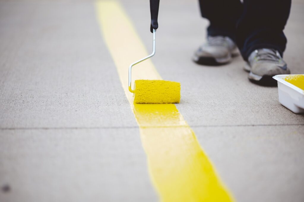 Une personne peignant une ligne jaune sur le sol en béton