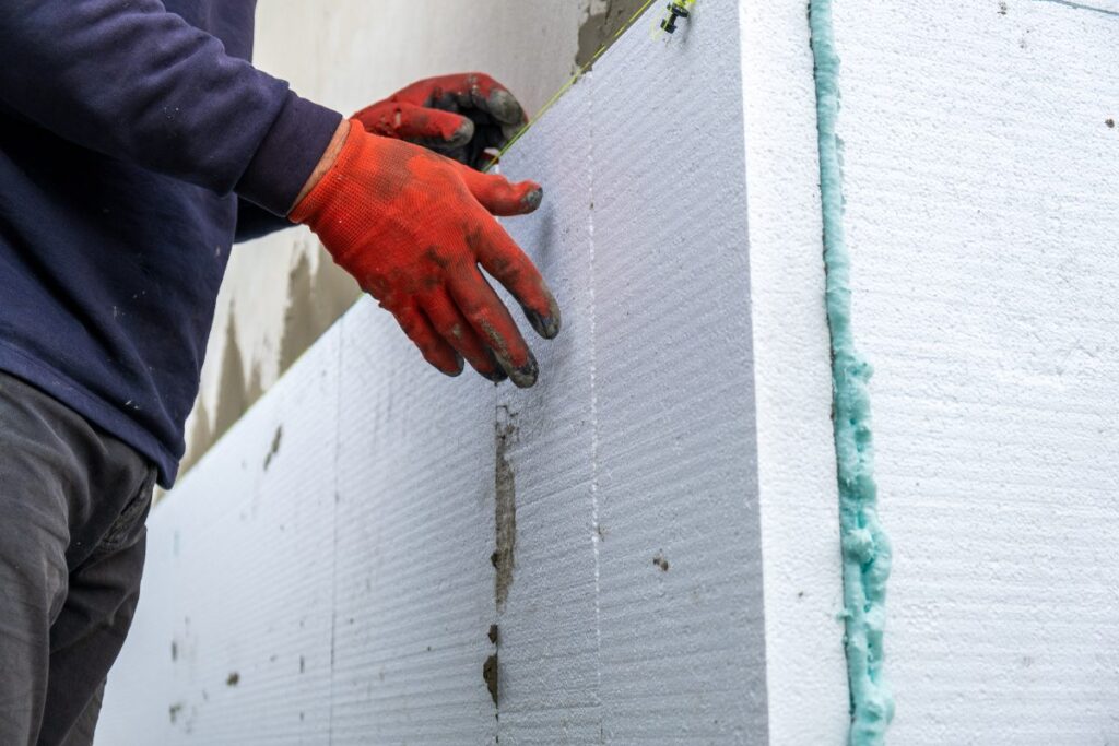 Un ouvrier du bâtiment installant des feuilles isolantes en polystyrène sur le mur